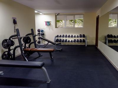 Nowoczesna siłownia z hantlami, ławką treningową i ścianą lustrzaną w jasnym pomieszczeniu.