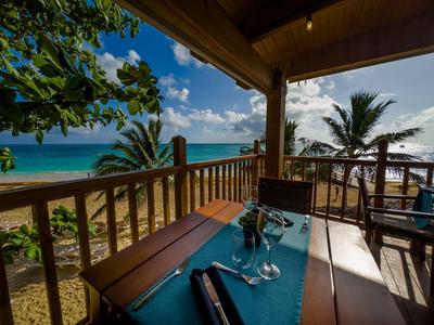 Vista da una terrazza coperta su una spiaggia con palme e mare blu.