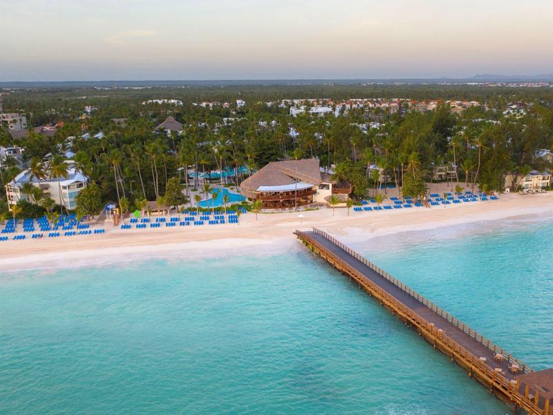Resort sulla spiaggia con molo di legno e ombrelloni blu sul mare turchese.