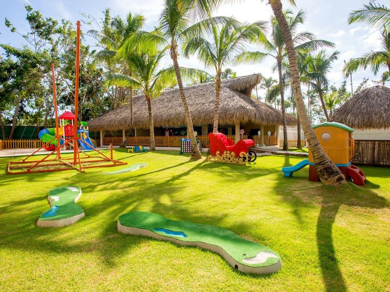 Area giochi con attrezzature colorate e palme su prato verde al sole.