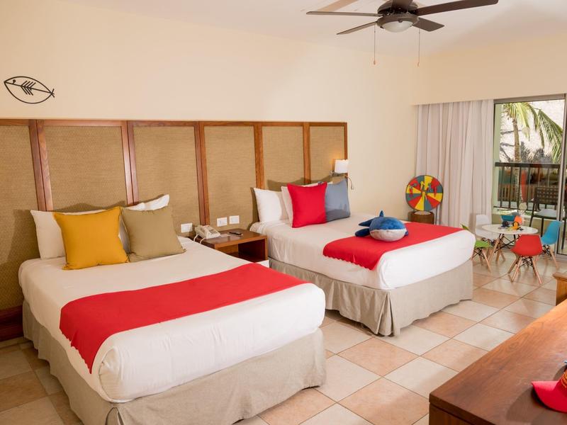 Camera d'hotel moderna con due letti singoli, cuscini colorati e terrazza con vista piscina.