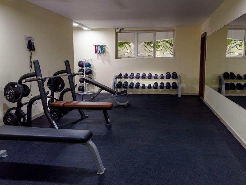 Piccola palestra con manubri, panca per esercizi e grandi specchi alle pareti.