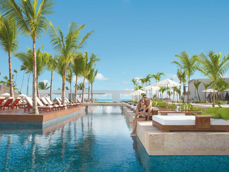 Moderner Außenpool mit Palmen, Liegen und klarem blauem Himmel an einem sonnigen Tag.