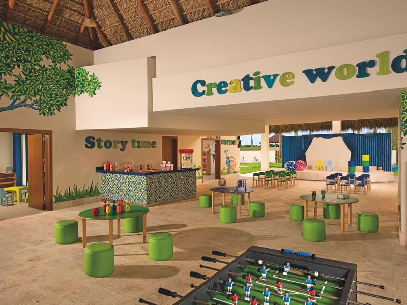 Heller, offener Raum mit grünen Sitzhockern, Kicker, Baumdeko und Schriftzug ?Creative world?.