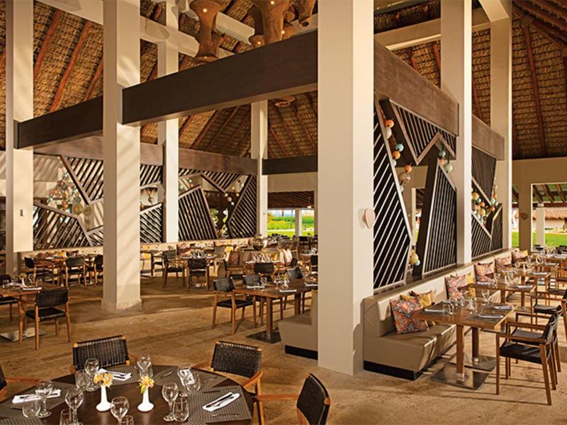 Großes Restaurant mit Holzdecken, weißen Säulen, vielen Tischen und Stühlen, warmes Licht.