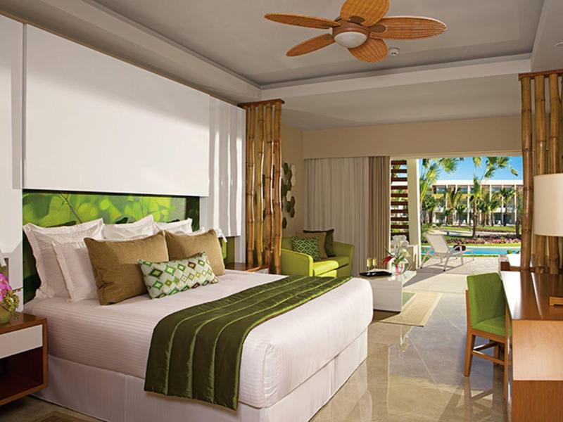 Modernes Schlafzimmer mit großem Bett, grüner Dekoration, Ventilator und Gartenblick durch große Fenster.