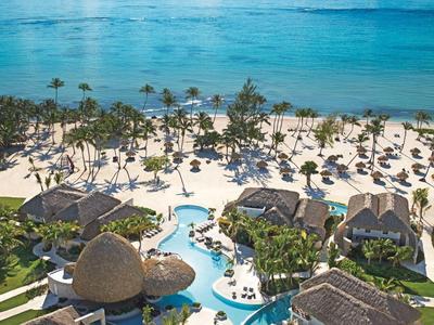 Uitzicht op een resort met zwembad, zandstrand en turquoise zee onder een blauwe lucht.