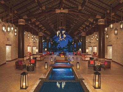 Zastřešená jídelní oblast s otevřeným koncem a centrální vodní dekorací, obklopená stoly a lampami.