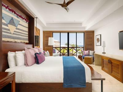 Modern hotelkamer met groot bed, kleurrijke kussens en uitzicht op balkon.