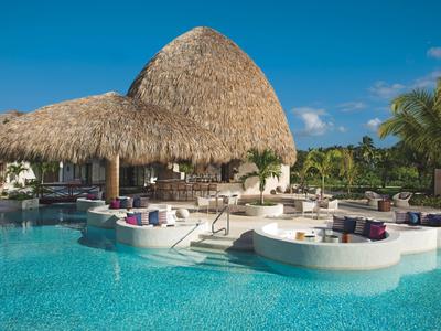 Groot zwembad met ingebouwd zitgedeelte en rieten dakbar in tropisch hotelresort.