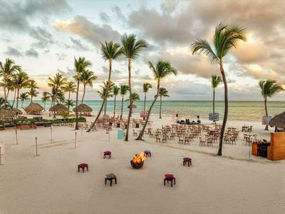 Sandstrand mit Palmen, Lagerfeuer und Sitzgelegenheiten nahe dem Meer unter bewölktem Himmel.
