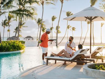 Personen entspannen am Pool unter Palmen bei Sonnenuntergang in einem tropischen Resort.