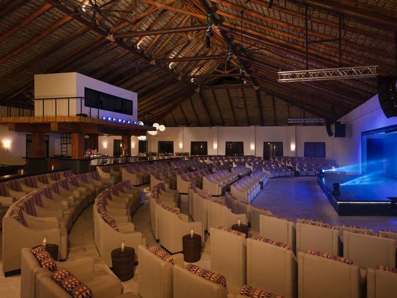 Grote evenementenzaal met vele zitrijen en een podium, sfeervol verlicht.