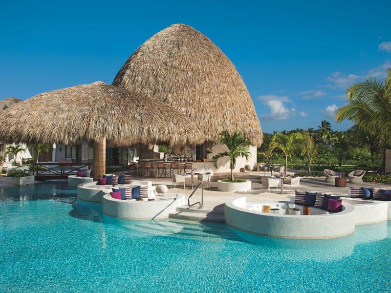 Groot zwembad met ingebouwd zitgedeelte en rieten dakbar in tropisch hotelresort.