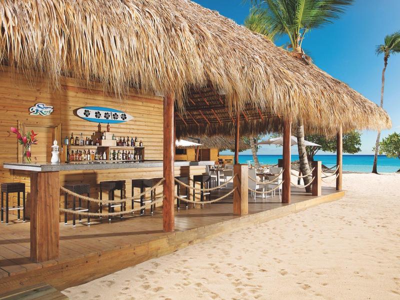 Beach bar with thatched roof and wooden furniture on white sandy beach by blue sea.