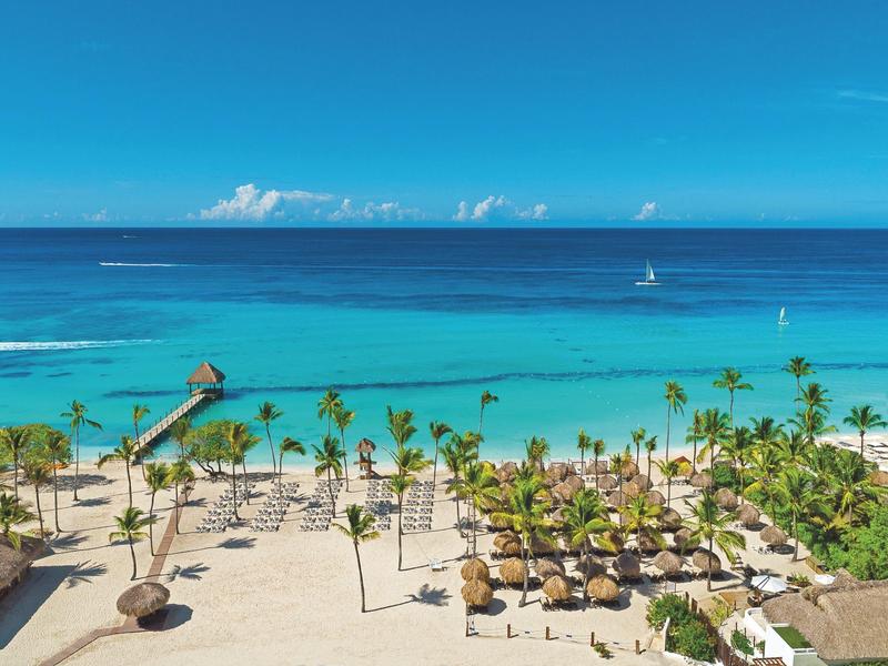 Beach with palm trees, sun umbrellas, and clear blue water under a blue sky.