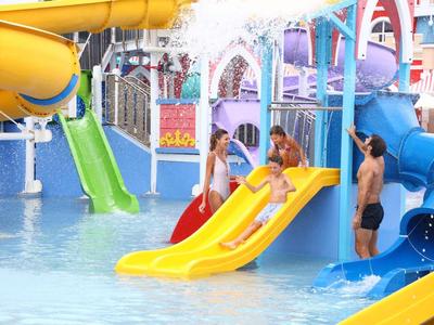 Kinder rutschen bunte Wasserrutschen im flachen Becken eines Wasserparks hinab.