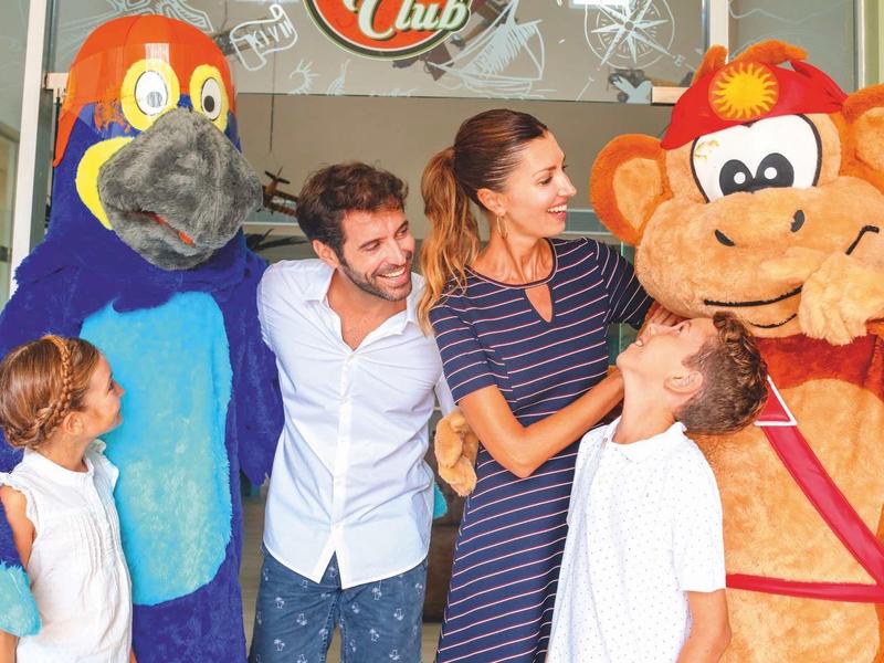 Eine Familie mit zwei Kindern steht fröhlich zwischen zwei bunten Maskottchen mit Tiermotiven.