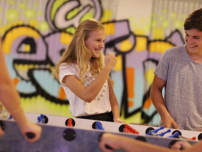 Junge und Mädchen spielen lachend Tischkicker mit bunten Figuren in hellem Raum.