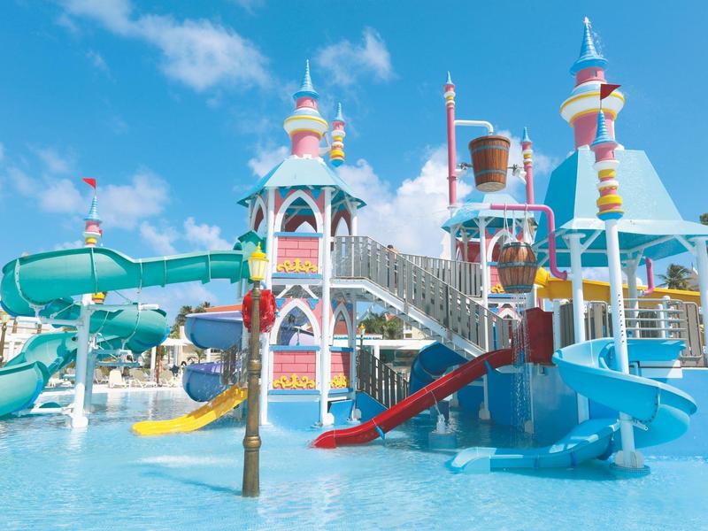 Buntes Wasserspielplatz mit Rutschen, Türmen und Wasserbecken unter blauem Himmel.