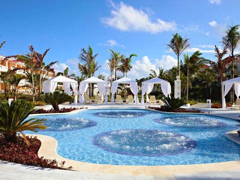 Luksusowy basen z białymi pawilonami i palmami pod błękitnym niebem.