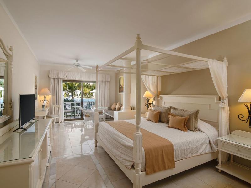 Jasny pokój hotelowy z łóżkiem z baldachimem, tarasem i widokiem na ogród.