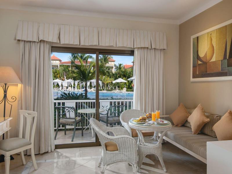 Jasny pokój z miejscem do siedzenia i widokiem na basen oraz palmy przez duże okna.