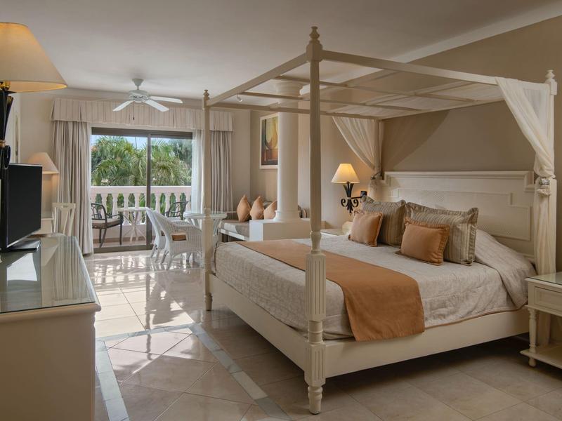Elegancki pokój hotelowy z łóżkiem baldachimowym, sofami i tarasem z widokiem na palmy.