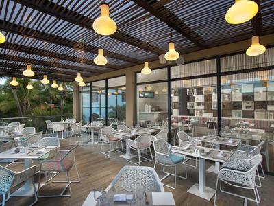 Modern outdoor restaurant area with multiple tables and chairs under a covered pergola.