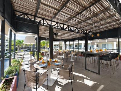 Covered outdoor area of a hotel restaurant with tables and chairs in a bright setting.