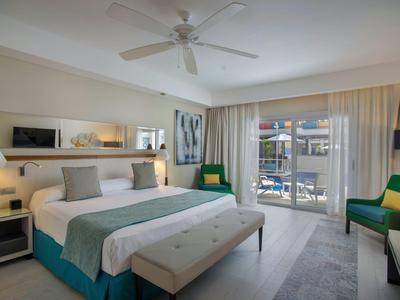 Modern hotel room with large bed, seating area, and balcony overlooking outdoors.