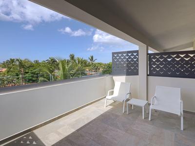 Balcony with two white chairs and table, view of green palms and blue sky.