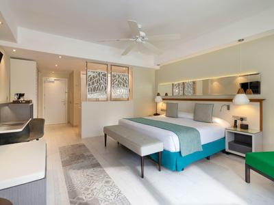 Modern hotel room with double bed, desk, TV, and green armchair.