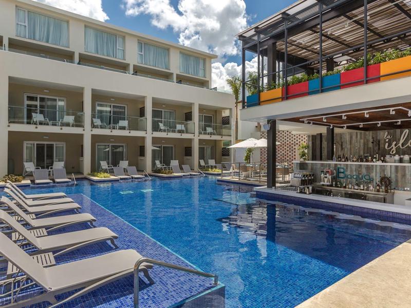 Modern hotel pool with lounge chairs and colorful bar under blue sky.