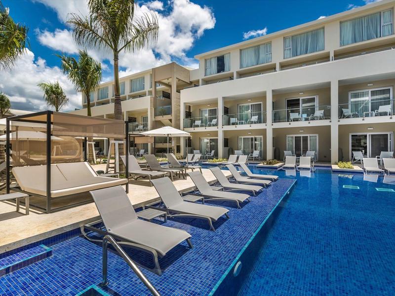 Modern hotel pool with lounge chairs and palm trees under a blue sky.