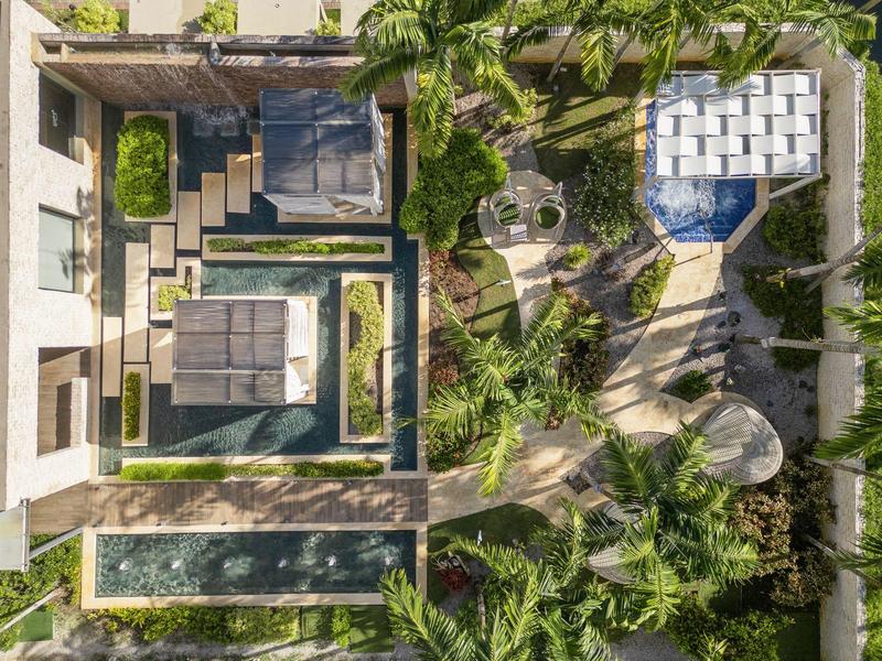 Aerial view of a modern hotel with pools and lush green vegetation.