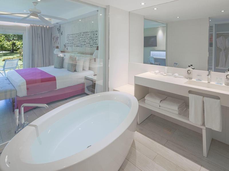 Modern hotel room with freestanding bathtub and double bed with pink covers.