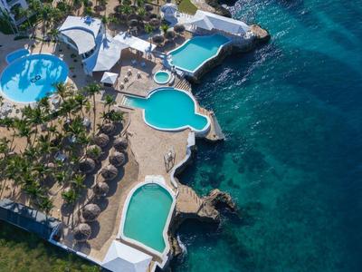 Luxusní hotelový komplex s několika bazény u moře a četnými palmami.