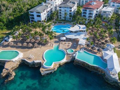 Luxusní hotelový resort s několika bazény přímo u moře, obklopený zelení.