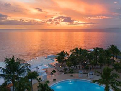 Západ slunce nad mořem s bazénem a palmami v tropickém resortu.