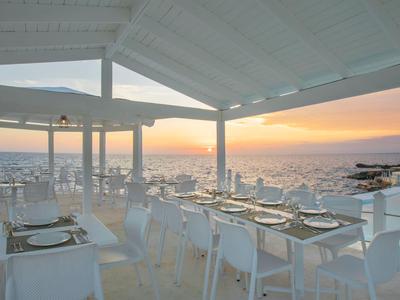 Open restaurant with white tables and chairs by the sea at sunset.