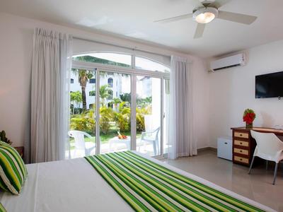 Světý hotelový pokoj s manželskou postelí, zelenými pruhovanými polštáři a přístupem do zahrady a ke bazénu.