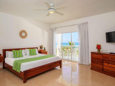 Světý hotelový pokoj s manželskou postelí, stropním ventilátorem, televizí a balkonem s výhledem na moře.