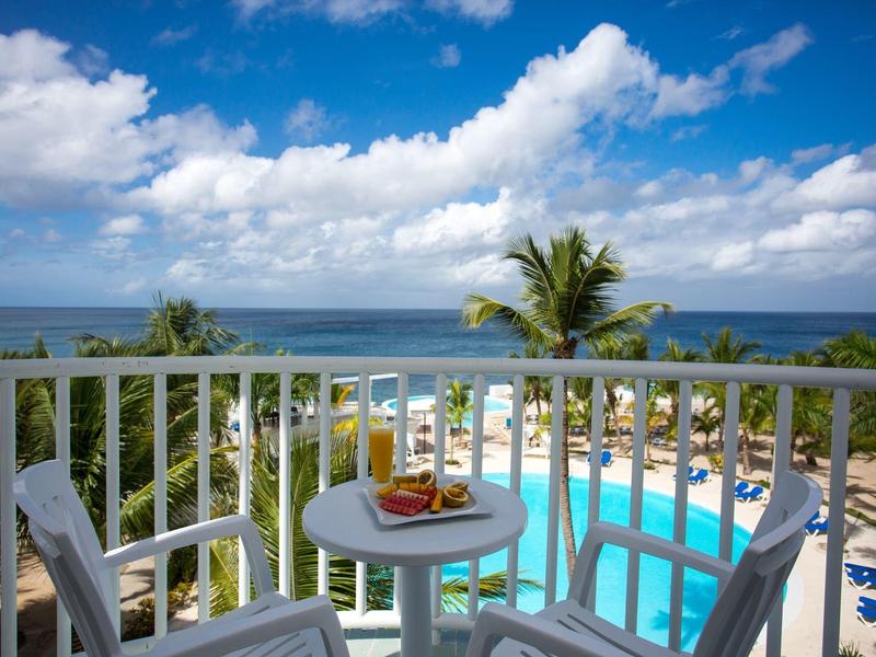 Výhled na bazén a moře z balkonu se stolem a dvěma židlemi.