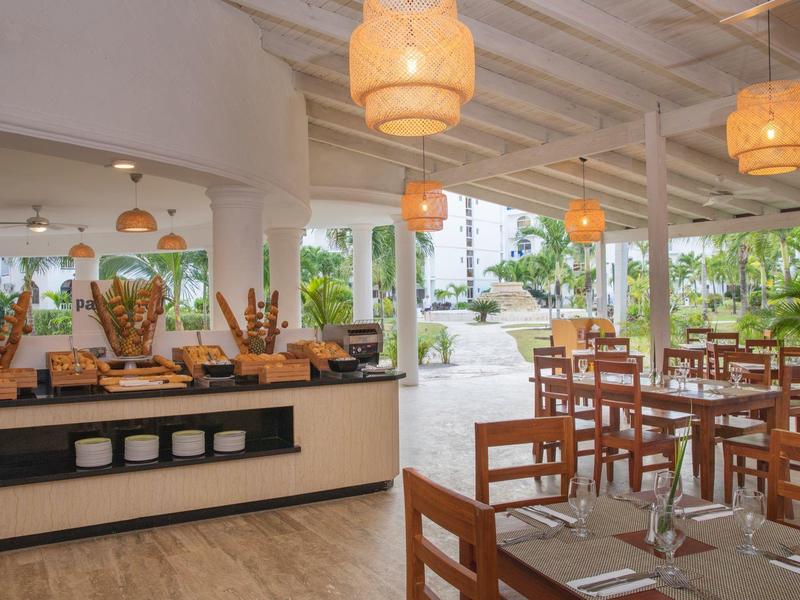 Otevřená restaurace se dřevěným nábytkem, bufetovou částí a výhledem na zelený venkovní prostor