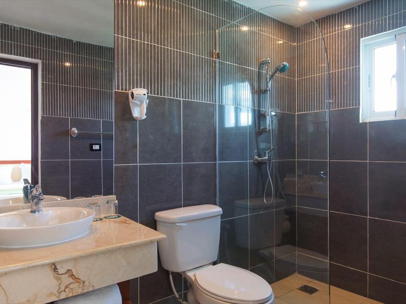 Moderní koupelna s tmavými dlaždicemi, sprchou, WC a umyvadlem se zrcadlem.