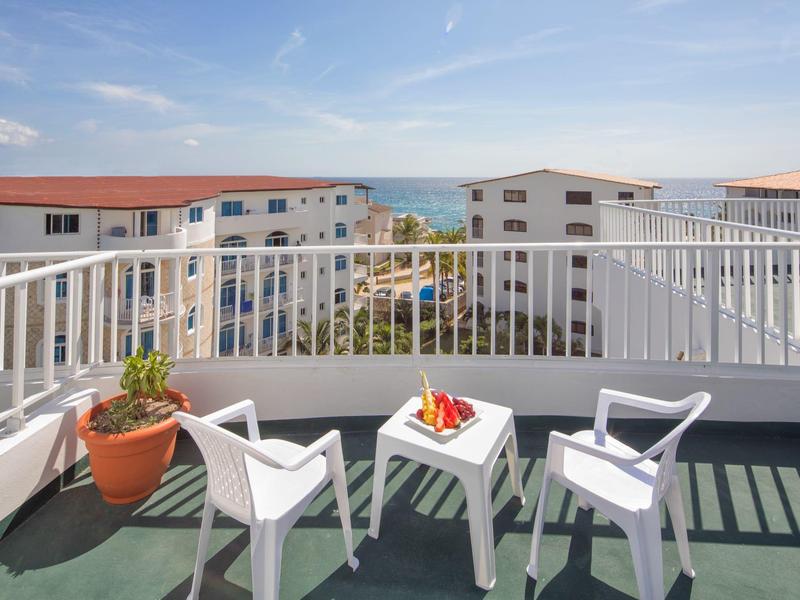Balkon s dvěma bílými židlemi, malým stolkem, výhledem na obytnou oblast a moře.