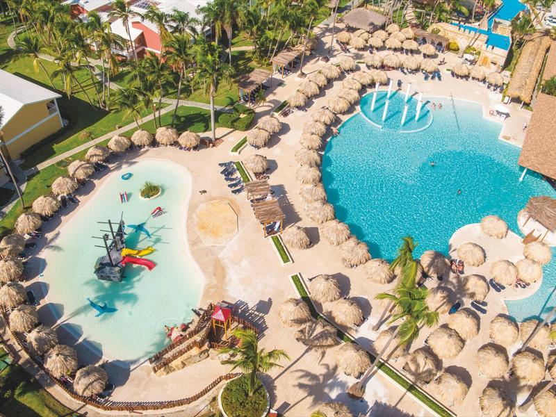Luchtfoto van een hotelzwembad met parasols en tropische omgeving.