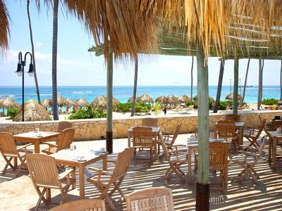 Otwarta przestrzeń do siedzenia z drewnianymi meblami i dachami ze słomy z widokiem na plażę i morze.