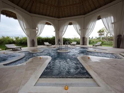 Zadaszony basen z kilkoma jacuzzi i białymi zasłonami w tropikalnym otoczeniu.